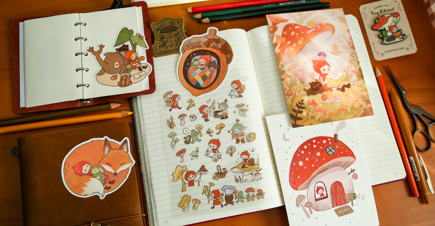 A notebook with Tiny Kikimo stickers on a wooden surface with stationery items.